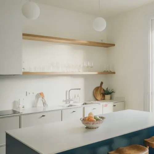 Estantes de madera en pared clara con platos, vasos, una cafetera y frascos, creando un espacio ordenado y práctico en la cocina