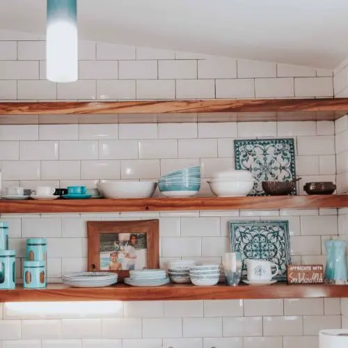 Estantes de madera con vajilla en tonos azules, colocados sobre una pared revestida de azulejos blancos en una cocina luminosa