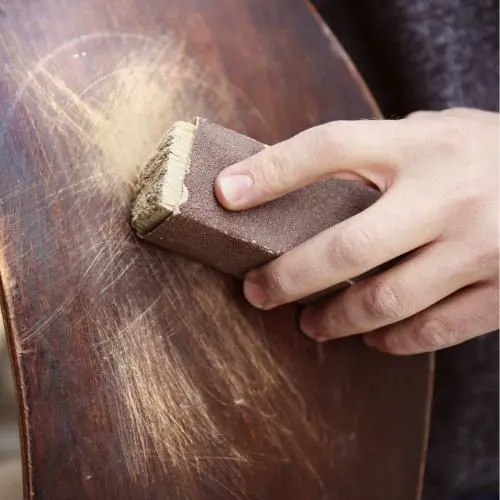 Mano lijando la superficie de un mueble de madera rayado para su restauración.