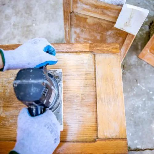 Carpintero utilizando una lijadora eléctrica para pulir un mueble de madera en proceso de restauración.
